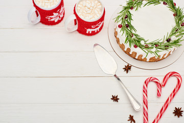 top view of christmas pie, candy canes and two cups of cocoa with marshmallows on white wooden table