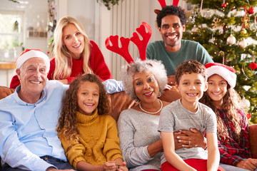 Portrait Of Multi-Generation Family Sitting On Sofa Celebrating Christmas Together