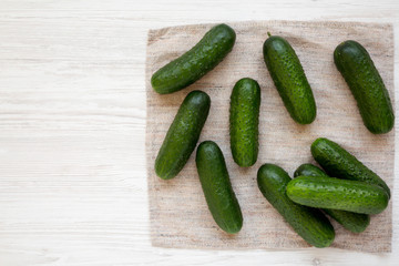 Ripe organic mini baby cucumbers on a white wooden background, top view. Flat lay, overhead, from above. Copy space.