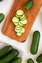 Fresh mini baby cucumbers on a rustic wooden board on a white wooden table, top view. Flat lay, overhead, from above. Close-up.