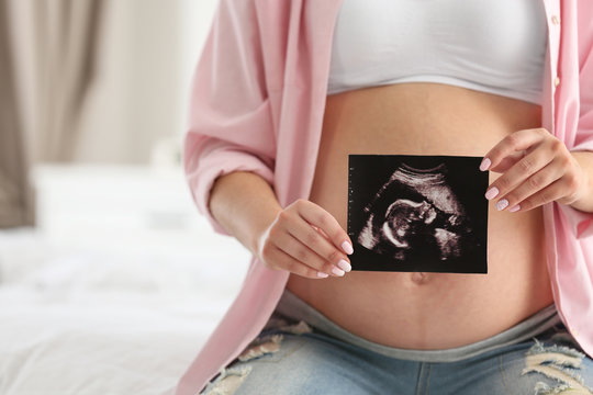 Pregnant woman with ultrasound picture indoors, closeup
