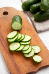 Chopped mini baby cucumbers on a rustic wooden board on a white wooden surface, low angle view. Close-up.