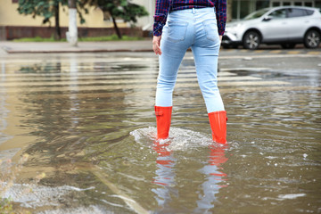 Woman with red rubber boots in puddle, closeup. Rainy weather