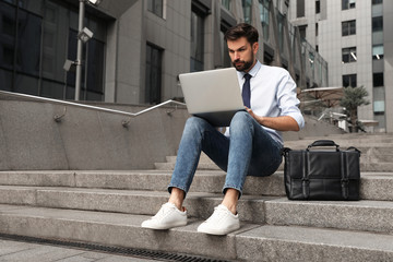 Handsome man working with laptop on city street