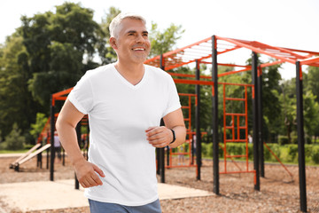 Handsome mature man running on sports ground, space for text. Healthy lifestyle