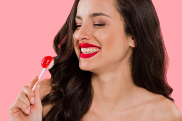 cheerful girl looking at sweet lollipop isolated on pink