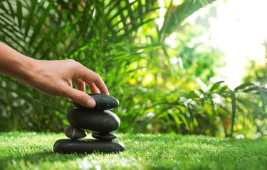 Woman stacking stones on green grass in garden, closeup. Space for text