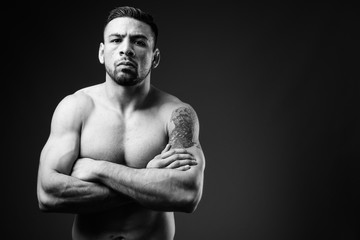 Young muscular Hispanic man shirtless against black background