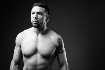 Young muscular Hispanic man shirtless against black background