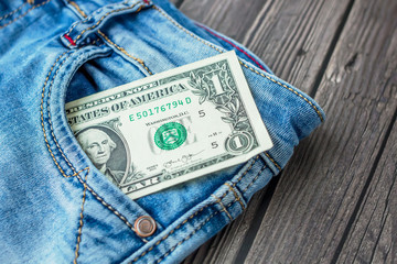 Dollar bill in jeans pocket on a dark wooden background. Top view, flat lay	