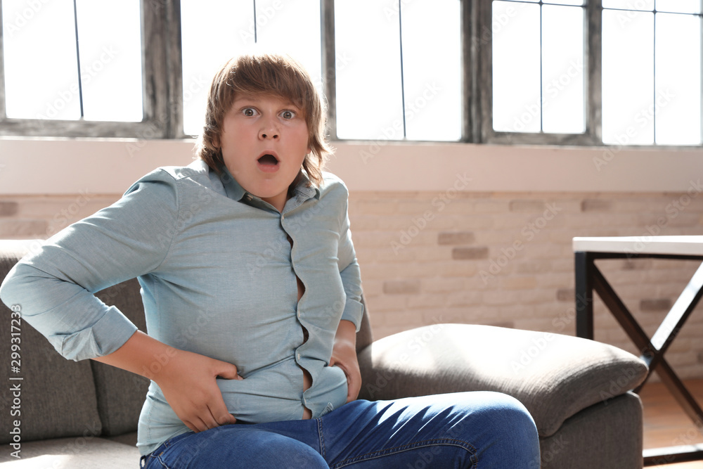 Sticker Emotional overweight boy sitting on sofa at home