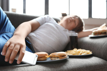 Overweight boy sleeping on sofa surrounded by fast food