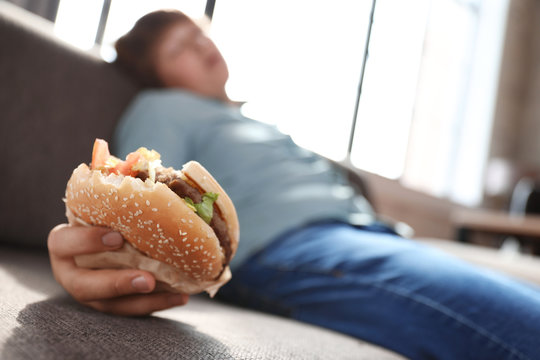 Overweight boy with burger sleeping on sofa at home