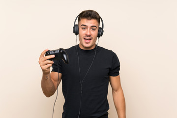 Young handsome man playing with a video game controller over isolated background with surprise and shocked facial expression
