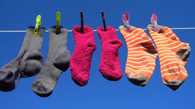 Close POV slow motion shot of a three pairs of colorful socks blowing gently in the breeze on an outdoor washing line, in the warm sunshine against a brilliant blue sky.