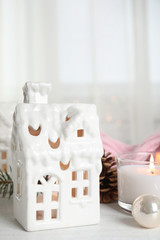 Fototapeta na wymiar Composition with candle in house shaped holder on white wooden table. Christmas decoration