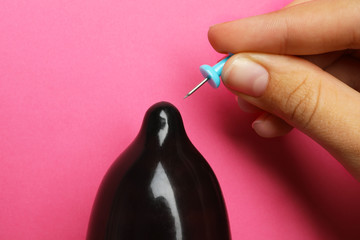 Woman piercing inflated condom with pin on pink background, closeup. Safe sex