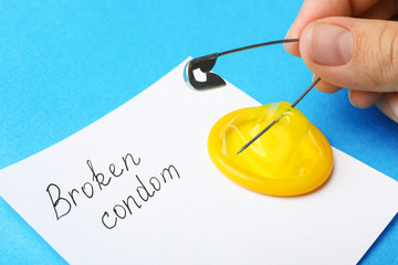 Woman piercing condom with pin on blue background, closeup. Safe sex
