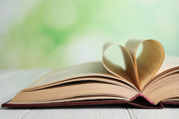 Open book on white wooden table against blurred green background, closeup