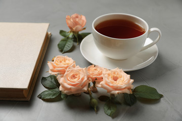 Fototapeta na wymiar Hardcover book, flowers and cup of tea on grey table