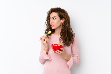 Young pretty woman over isolated background holding a bowl of cereals and thinking