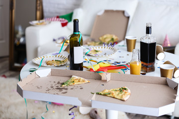 Messy table with bottles and pizza indoors. Chaos after party