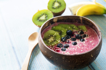 Bowl with yummy berry smoothie on blue wooden table. Healthy vegan food concept.