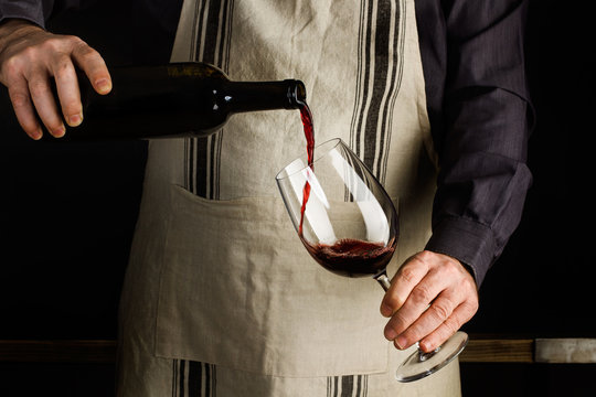Hombre vertiendo vino tinto en una copa de vino. Sommelier vierte bebida alcoh&oacute;lica - Vista de frente y de cerca