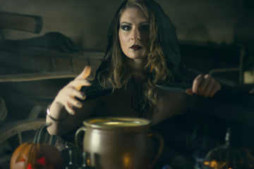 Beautiful witch in black mantle with a pumpkin and magical things on Halloween celebration