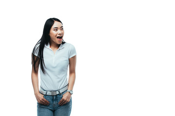 excited attractive asian girl with hands in pockets and open mouth looking away isolated on white