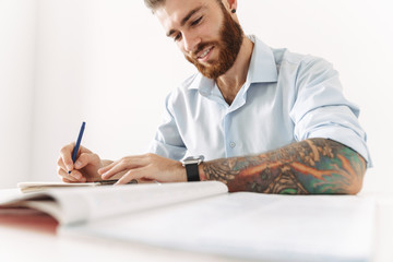 Image of brunette man sitting at table and studying with exercise books