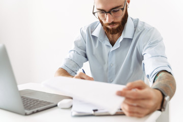 Image of man in eyeglasses working on laptop with documents in office