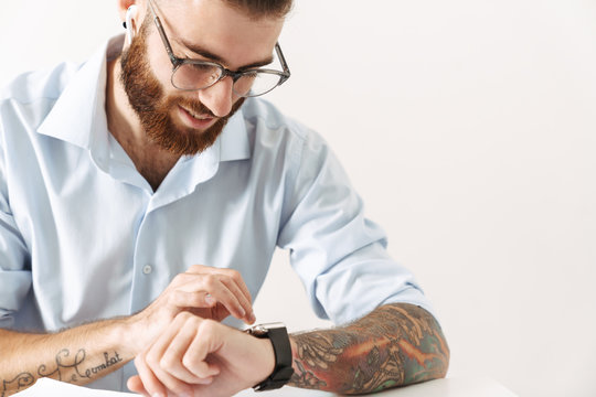 Image of young man looking at wristwatch while working at table in office