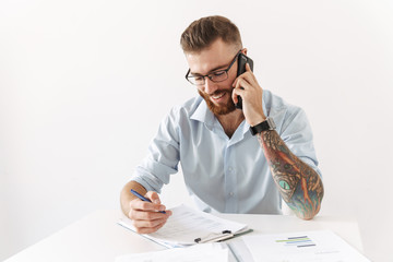 Image of unshaven young man talking on smartphone while working in office