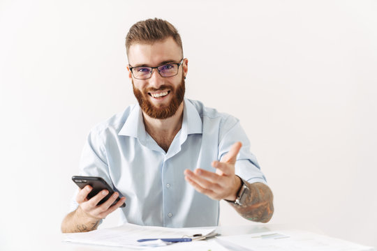 Image of bearded young man holding smartphone while working in office