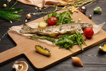 fried trout with arugula, cherry tomatoes and lemon on a board