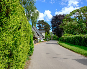 Quintessential view of a typical English village showing an empty narrow road with cottages together with a distant cyclist on a summers day.