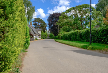 Quintessential view of a typical English village showing an empty narrow road with cottages together with a distant cyclist on a summers day.