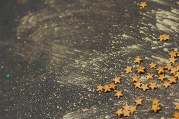 confectionery confetti in the shape of gold stars on a dark gray background with space for text. decor for Christmas baking.	