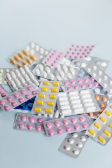 Various medicaments: white, pink and yellow pharmaceutical medicine pills, a remedy for flu, headache pills, antibiotics. Medical and healthcare concept. Cropped vertical photo, soft focus.