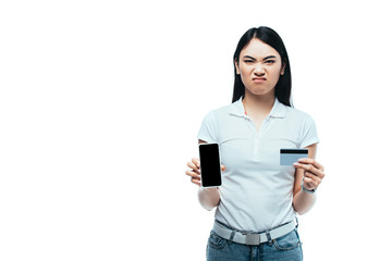 displeased brunette asian girl holding credit card and smartphone with blank screen isolated on white