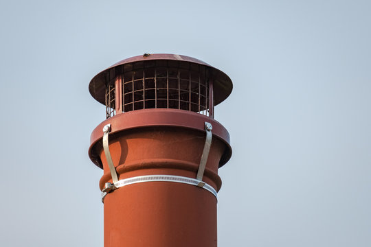 Isolated view of an old fashioned, terracotta chimney pot seen on a cottage roof, against a clear sky. The pot is capped off to prevent birds nests blocking up this word burning chimney.