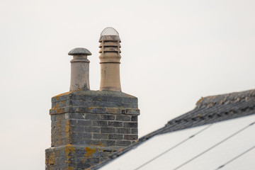 Isolated view of a newly install Solar Panel on a house roof, in contrast to a very old Chimney used for wood burnin, one giving no emissions, the other creating pollutant
