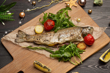 fried trout with arugula, cherry tomatoes and lemon on a board