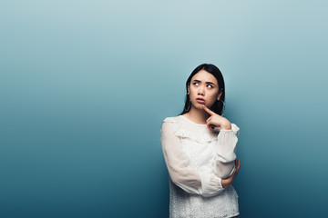 thoughtful brunette asian woman looking away on blue background