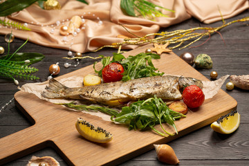 fried trout with arugula, cherry tomatoes and lemon on a board