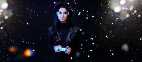 Fototapeta premium Beautiful woman with joystick in glasses of virtual reality on dark magic background. Augmented reality, future technology concept. VR. Futuristic 3d glasses with virtual projection. Blue neon light.
