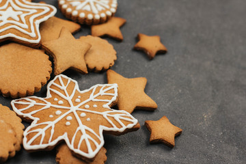 Fototapeta na wymiar Gingerbread cookie in the shape of stars, circles and snowflakes on a dark gray background with space for text. Christmas cookies with icing decor.