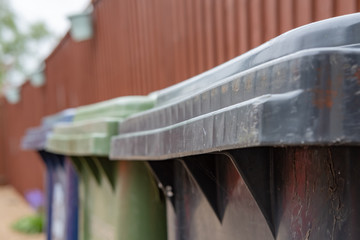  Close up, shallow focus of a green plastic wheelie bin used for organic waste collection seen next to a wooden garden fence in a back garden.