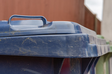  Close up, shallow focus of a green plastic wheelie bin used for organic waste collection seen next to a wooden garden fence in a back garden.